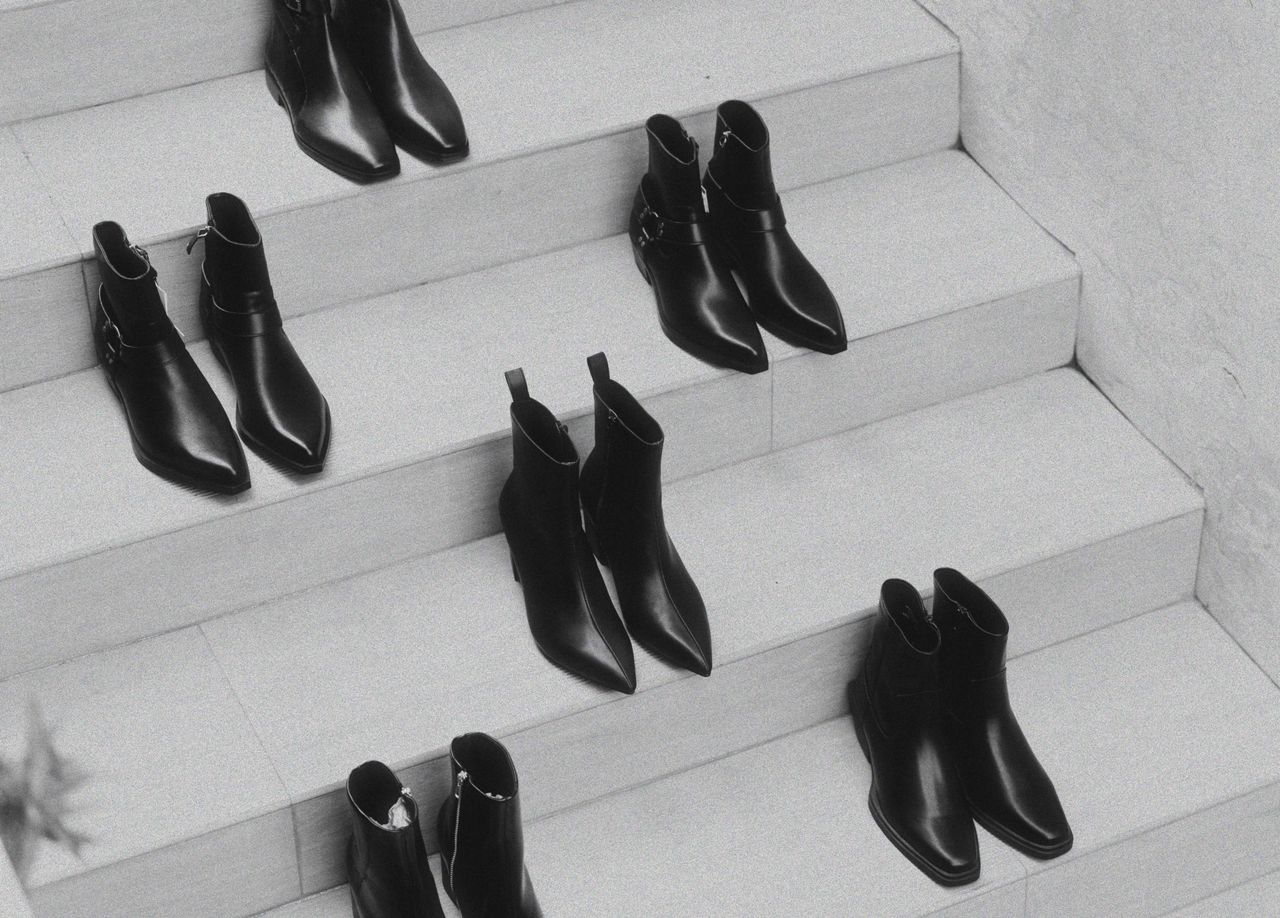 A stylish arrangement of black leather boots on a white staircase, emphasizing fashion and minimalism.
